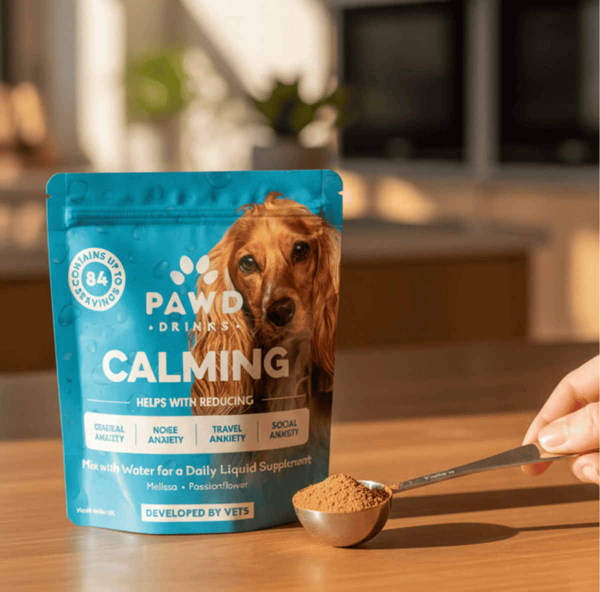 A hand holds a spoonful of brown powder next to a bag of Pawd Drinks Calming dog supplement.